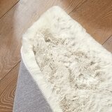 Folded cream faux fur rug with thick, fluffy texture on wooden floor