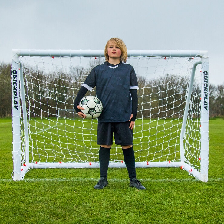 Lifestyle image of a goalkeeper stood in from of the goal, holding a ball