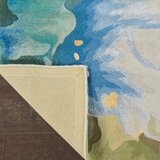 Corner of a patterned rug folded to show the plain beige underside. The top has a colourful abstract design in blue, green, and yellow.