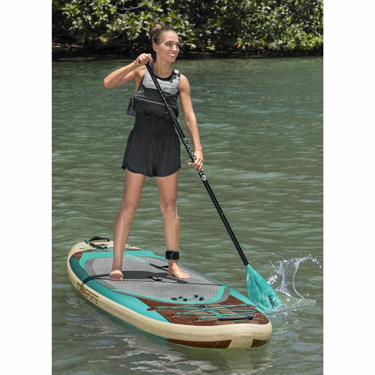 Lifestyle image of a woman stoood on the paddleboard, paddle in hand