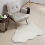 White lambskin-style rug with an irregular, cloud-like shape and soft, fluffy texture on a light wooden floor