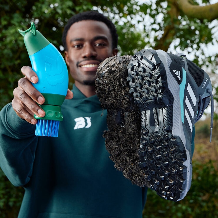 Lifestyle image of someone holding the boot buddy, a dirty shoe and a clean shoe