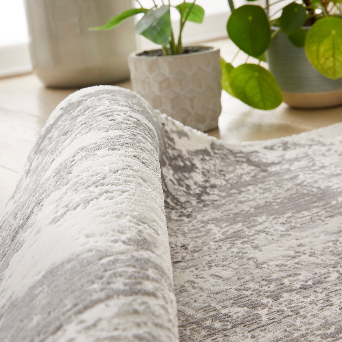 Textured rug with a distressed abstract pattern in grey, cream and light brown, showing irregular brushstroke-style detailing.