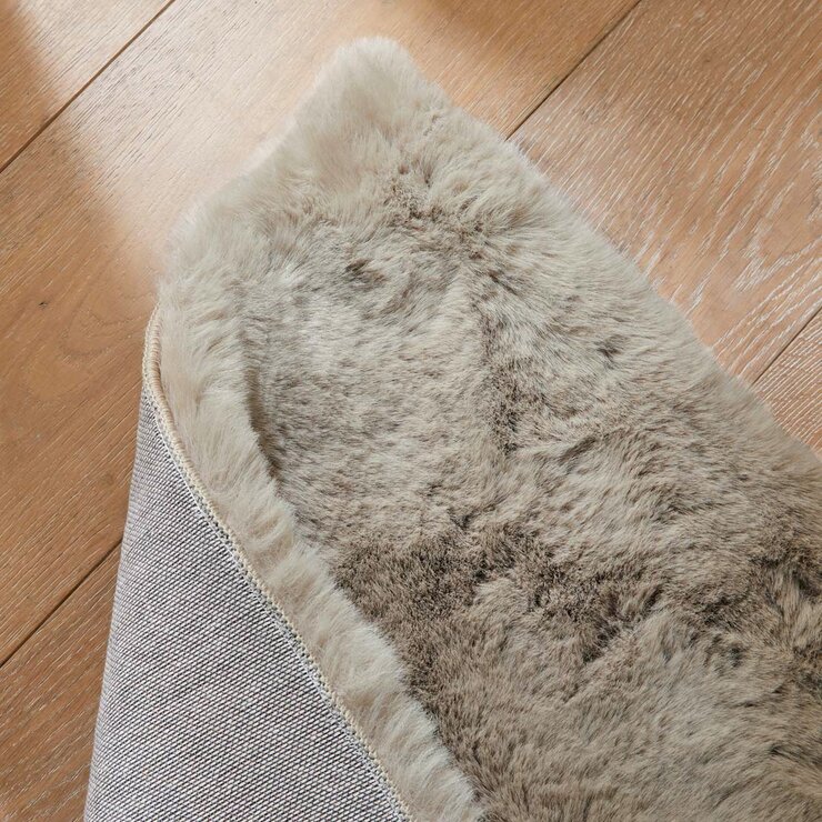 Folded taupe faux fur rug with thick, fluffy texture on wooden floor Folded taupe faux fur rug with thick, fluffy texture on wooden floor