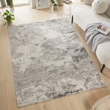 Large grey and cream rug with a distressed abstract pattern, placed in a modern living room with light wood flooring and minimal decor.