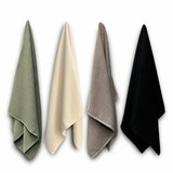 Four textured bath sheets in green, cream, taupe, and black, hanging vertically against a white background