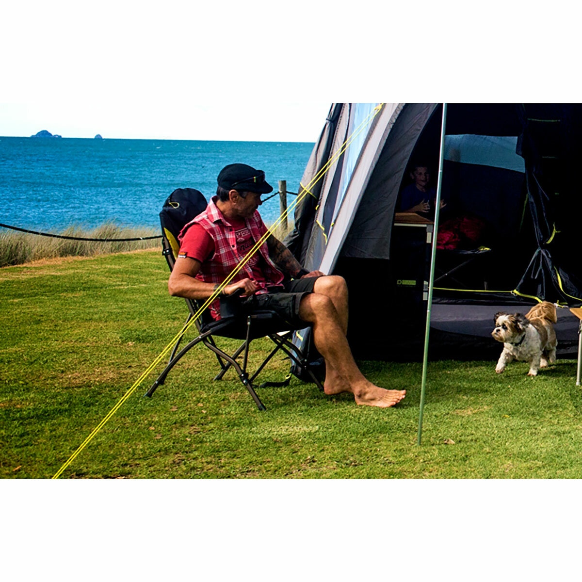Lifestyle image of a man sat in the chair next to a tent Lifestyle image of a man sat in the chair next to a tent