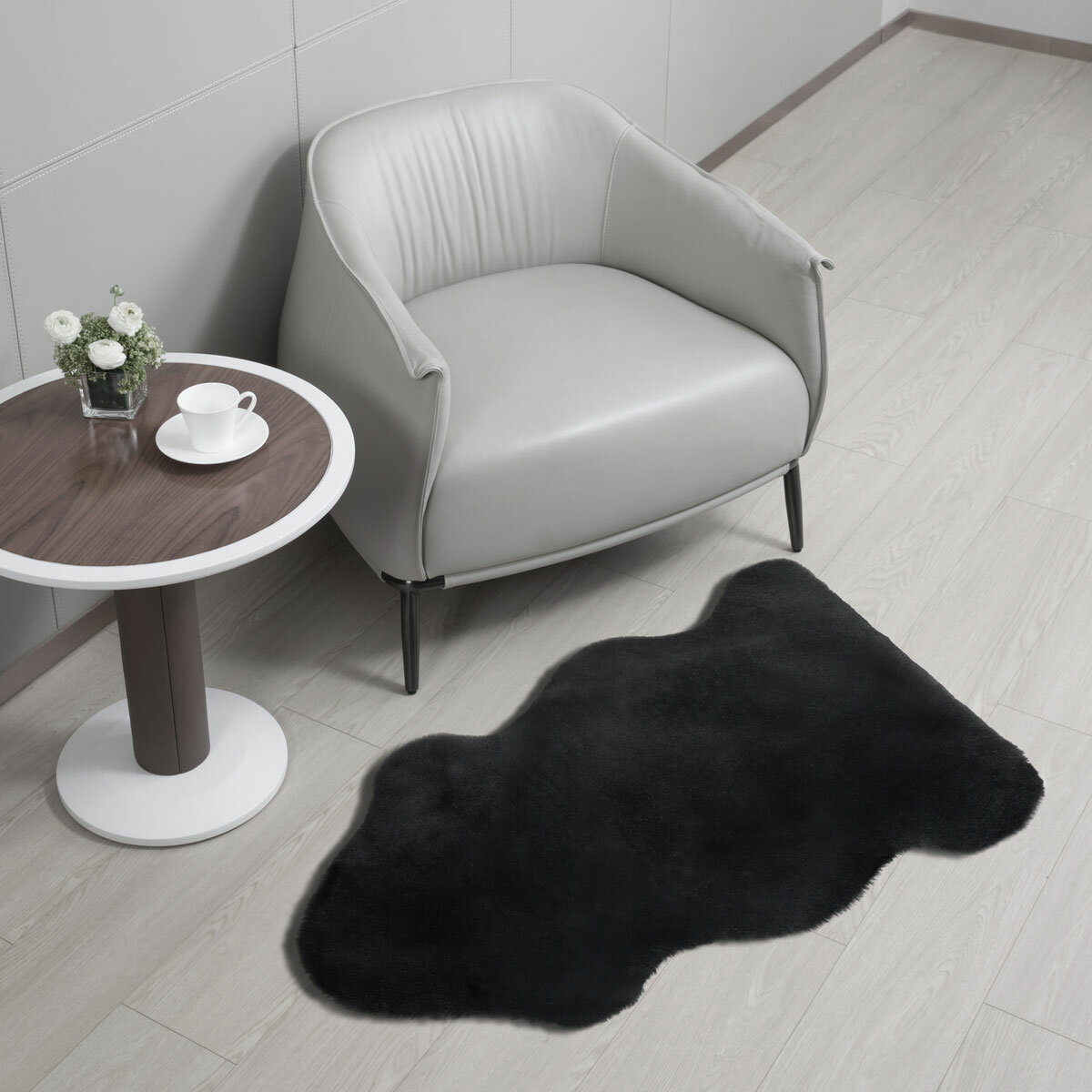 Black lambskin-style rug with an irregular, cloud-like shape and soft, fluffy texture on a light wooden floor