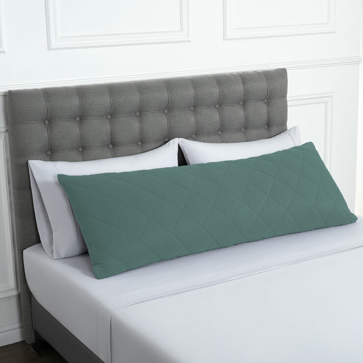 Quilted green body pillow with diamond stitching placed in front of two white pillows on a neatly Quilted green body pillow with diamond stitching placed in front of two white pillows on a neatly
