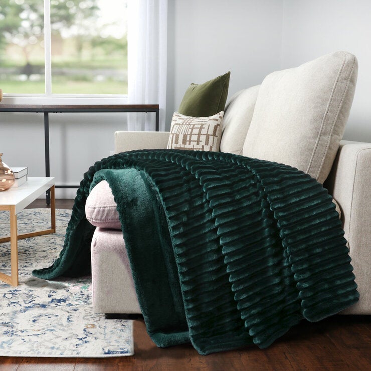 Dark green ribbed throw blanket draped over a cream armchair in a cosy living room Dark green ribbed throw blanket draped over a cream armchair in a cosy living room