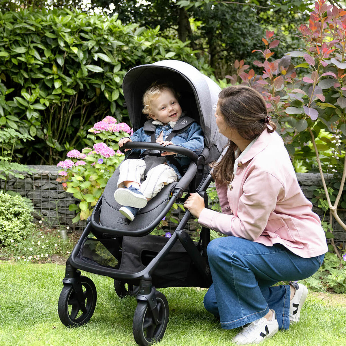 Lifestyle image of a woman crouched next to the stroller, looking at her baby