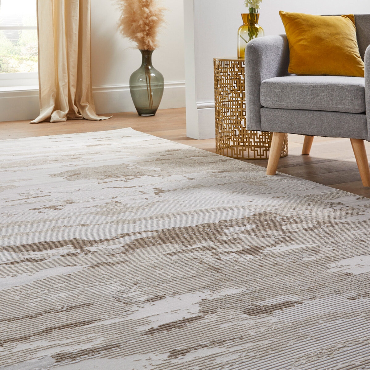 Beige and white abstract rug under a grey armchair and gold side table in a cosy corner setup.
