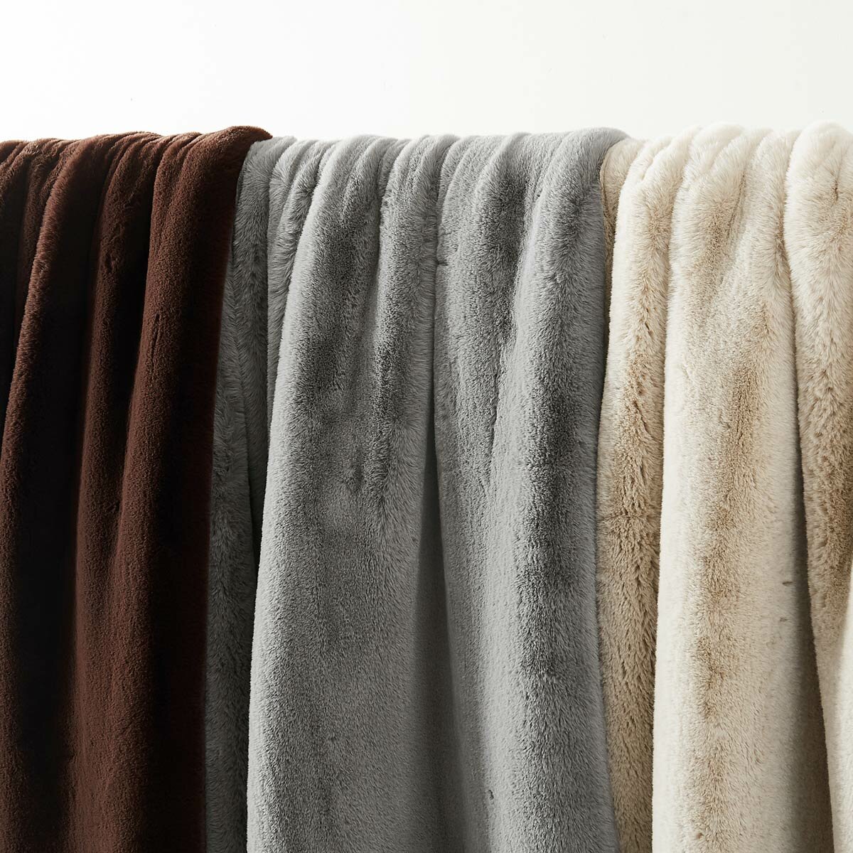 Three faux fur throws in brown, grey and beige hanging side by side