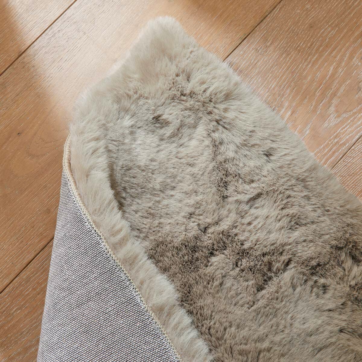 Folded taupe faux fur rug with thick, fluffy texture on wooden floor Folded taupe faux fur rug with thick, fluffy texture on wooden floor