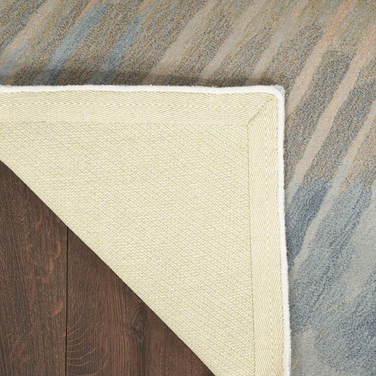 Gradient rug in blue, grey and beige, shown flipped to reveal a light beige herringbone backing with stitched edges.