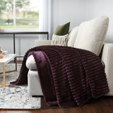 Purple ribbed throw blanket draped over a cream armchair in a cosy living room Purple ribbed throw blanket draped over a cream armchair in a cosy living room