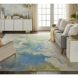 Large rug with a soft abstract pattern in blue, green, beige, and white. Shown in a cosy living room with a grey sofa and neutral decor.