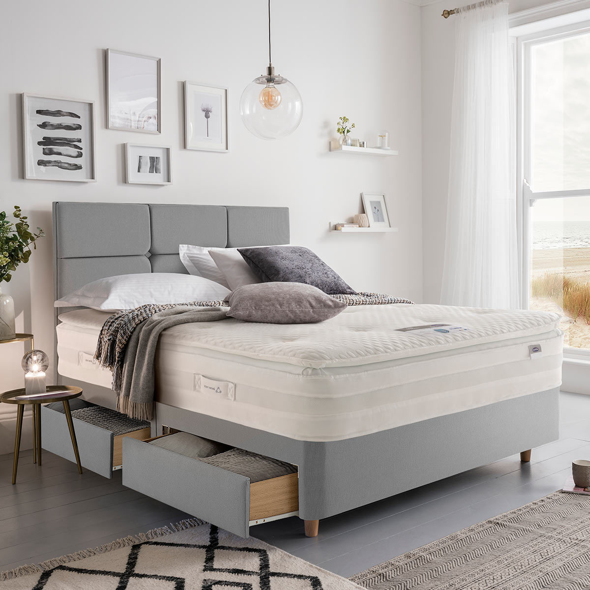 Lifestyle image of made up bed in slate in front of window showing beachside