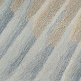 Rug with a sand-like texture and wavy bands in light blue, grey and beige, creating a dynamic, brushstroke-style pattern.