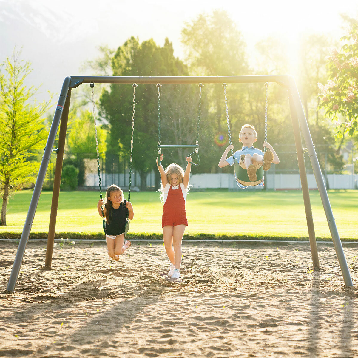 Lifestyle image of two children on the swings and one child hanging from the trapeze bar Lifestyle image of two children on the swings and one child hanging from the trapeze bar