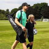Lifestyle image of a man carrying the goal in the bag, his arm on the shoulder of a child walking next to him with the football