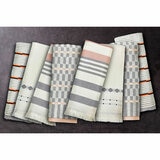 Set of eight folded woven tea towels in grey, beige and orange geometric and striped patterns, arranged to show their weave and detail