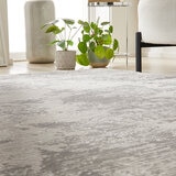 Grey-toned rug with a soft abstract design in grey and cream, styled with a white sofa and gold side table on light wood flooring.