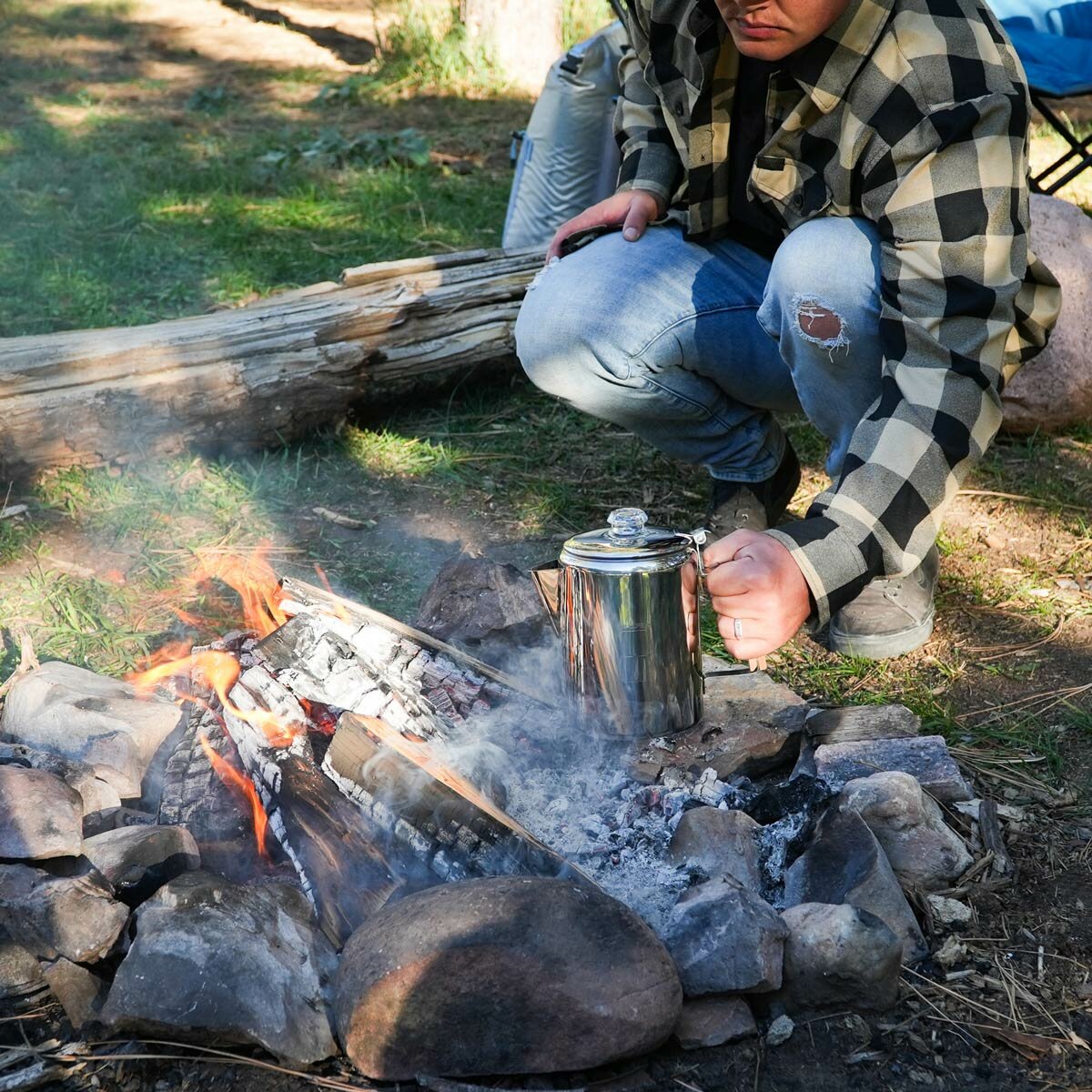 A lifestyle image of someone putting the percolator onto a campfire