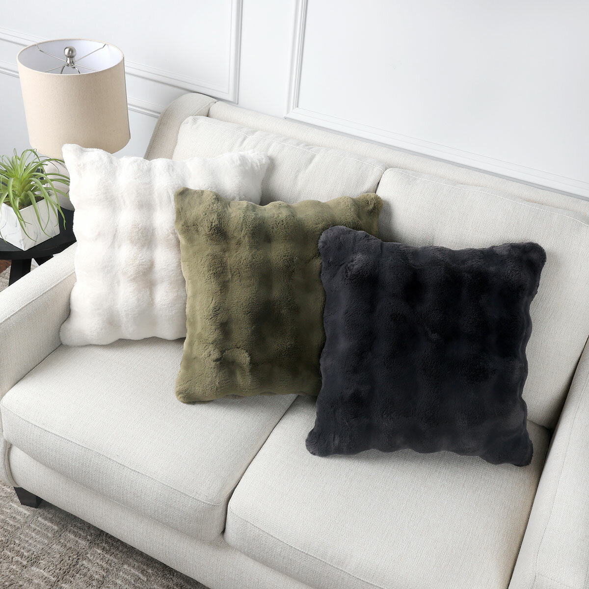 Three square cushions on a beige sofa: white, olive green, and dark grey, each with a bubble texture Three square cushions on a beige sofa: white, olive green, and dark grey, each with a bubble texture