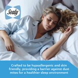 A fitted white mattress protector with a hexagonal quilted pattern on a neatly made bed in a modern bedroom