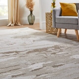 Beige and white abstract rug under a grey armchair and gold side table in a cosy corner setup.