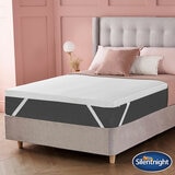A white mattress topper with elastic corner straps fitted neatly over a mattress.