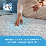A fitted white mattress protector with a hexagonal quilted pattern on a neatly made bed in a modern bedroom