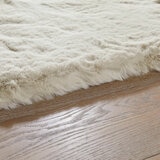 Cream faux fur rug with thick, fluffy texture on wooden floor