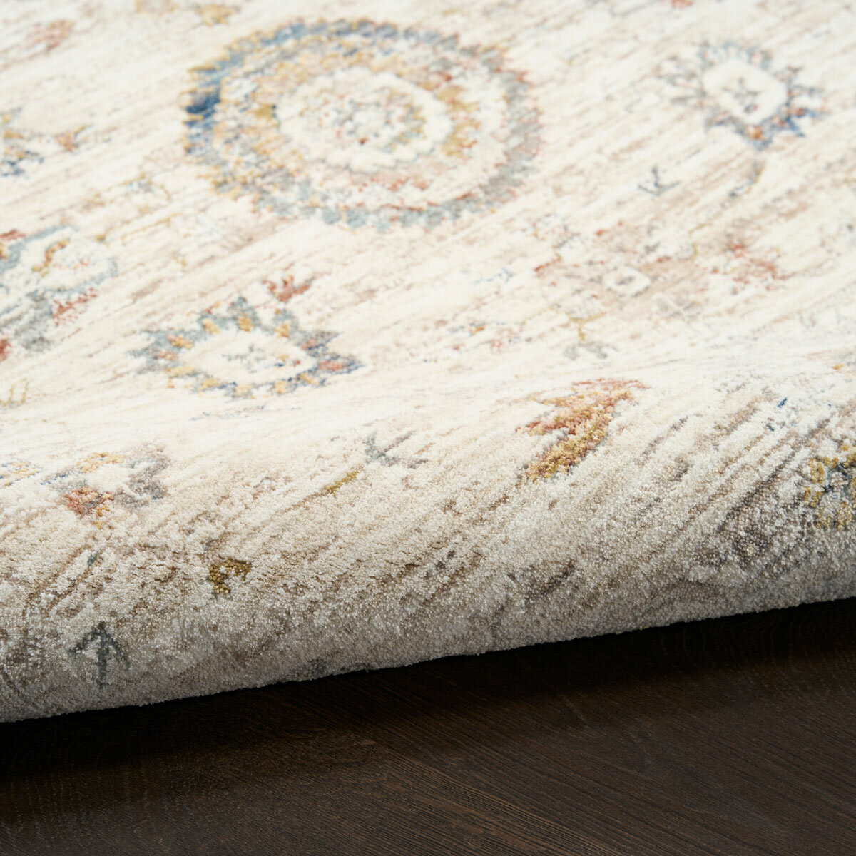 Beige rug with symmetrical floral and geometric pattern in muted blue, red, yellow, and grey