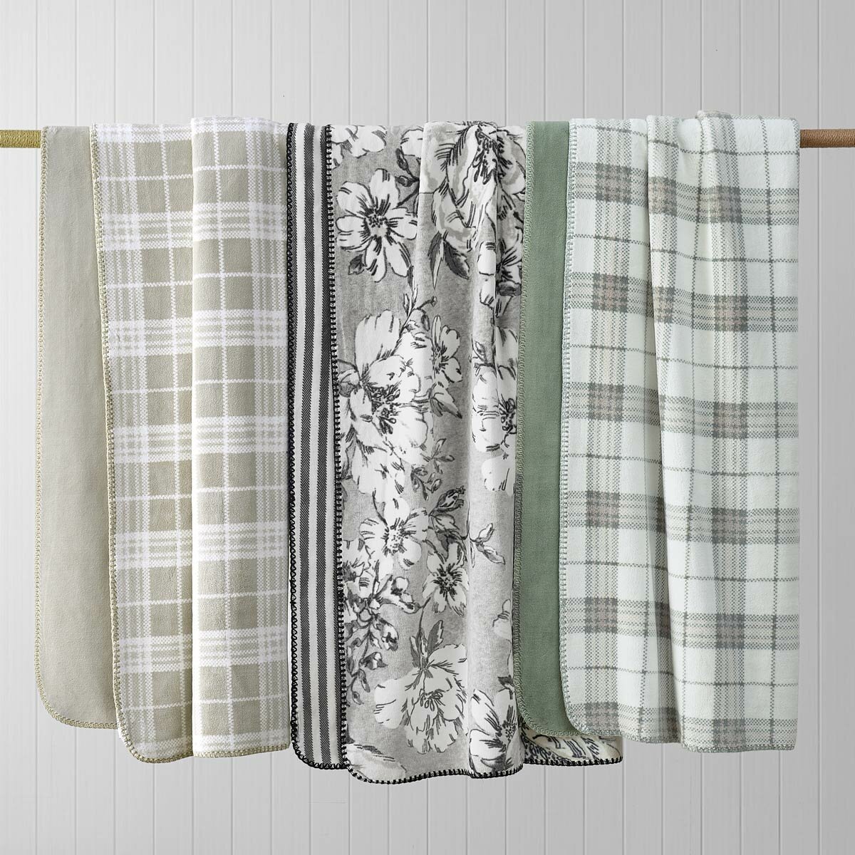 Plaid and floral throws in colours: Sage green, Taupe and black + white staged on a rail Plaid and floral throws in colours: Sage green, Taupe and black + white staged on a rail