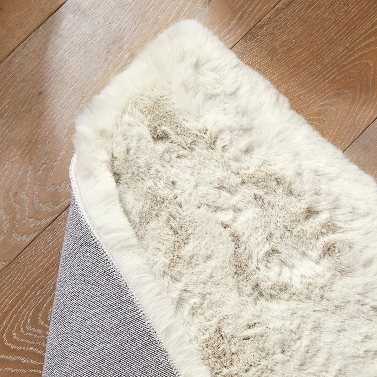 Folded cream faux fur rug with thick, fluffy texture on wooden floor