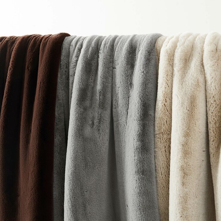 Three faux fur throws in brown, grey and beige hanging side by side