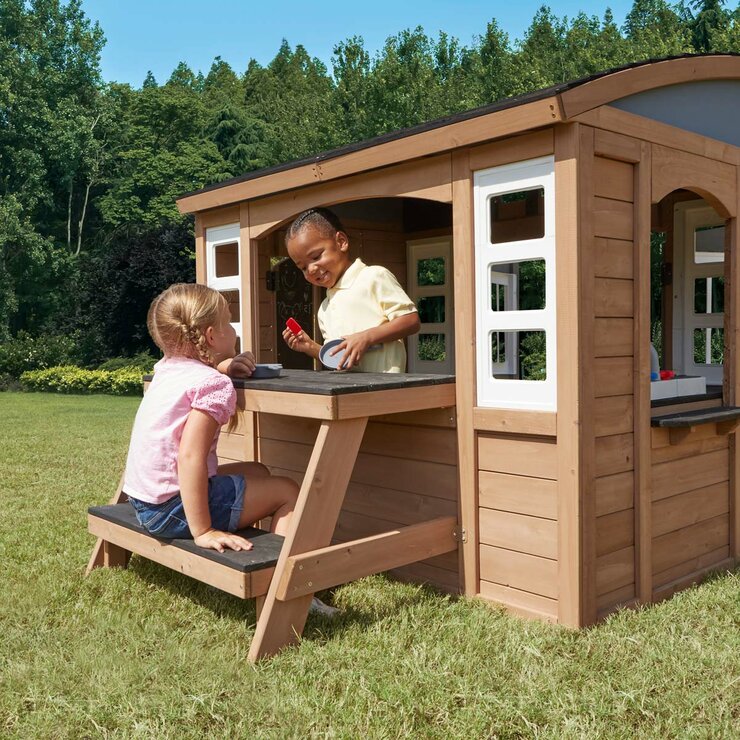 Lifestyle image of a child sat at the picnic area and another child in the playhouse