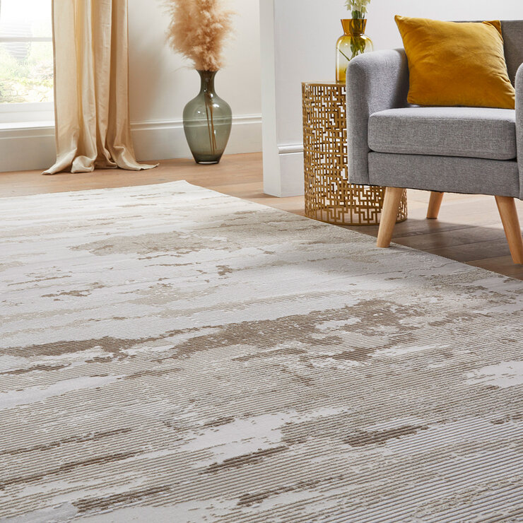 Beige and white abstract rug under a grey armchair and gold side table in a cosy corner setup.
