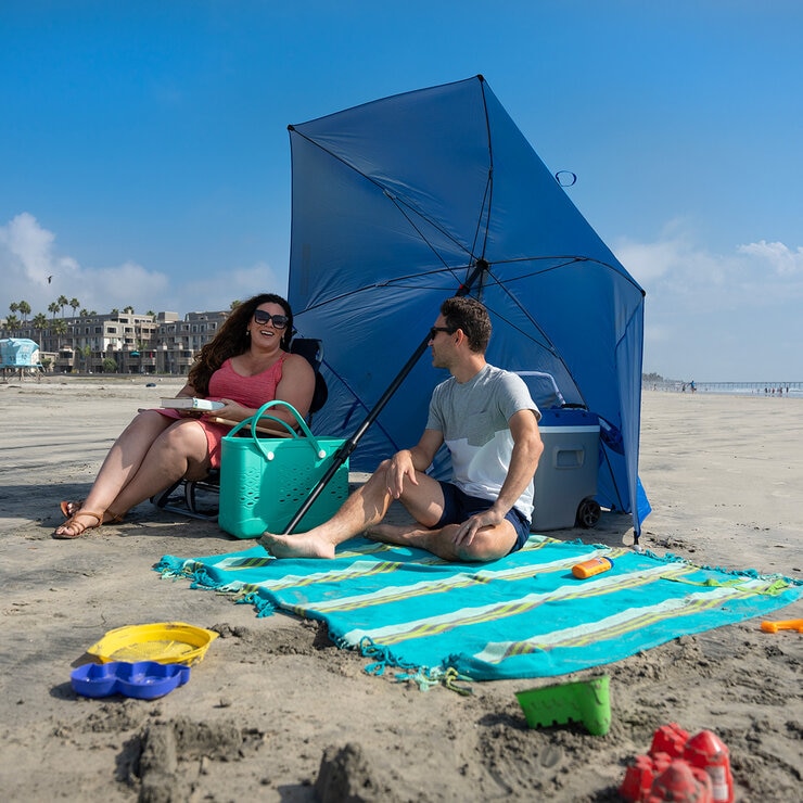 Lifestyle image of two people sat on the beach underneath the shelter