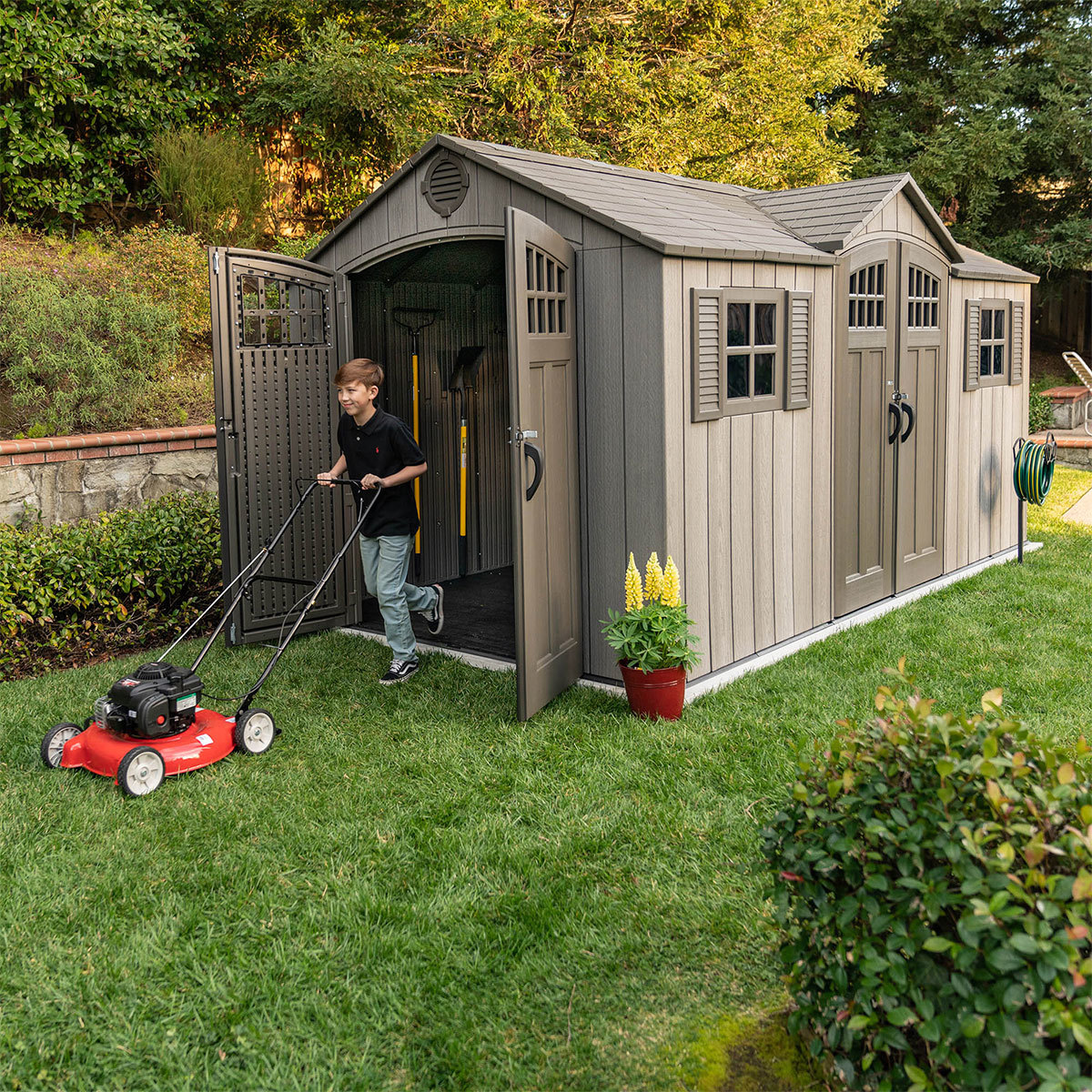 Boy walking out of lifetime Storage shed with a lawnmower