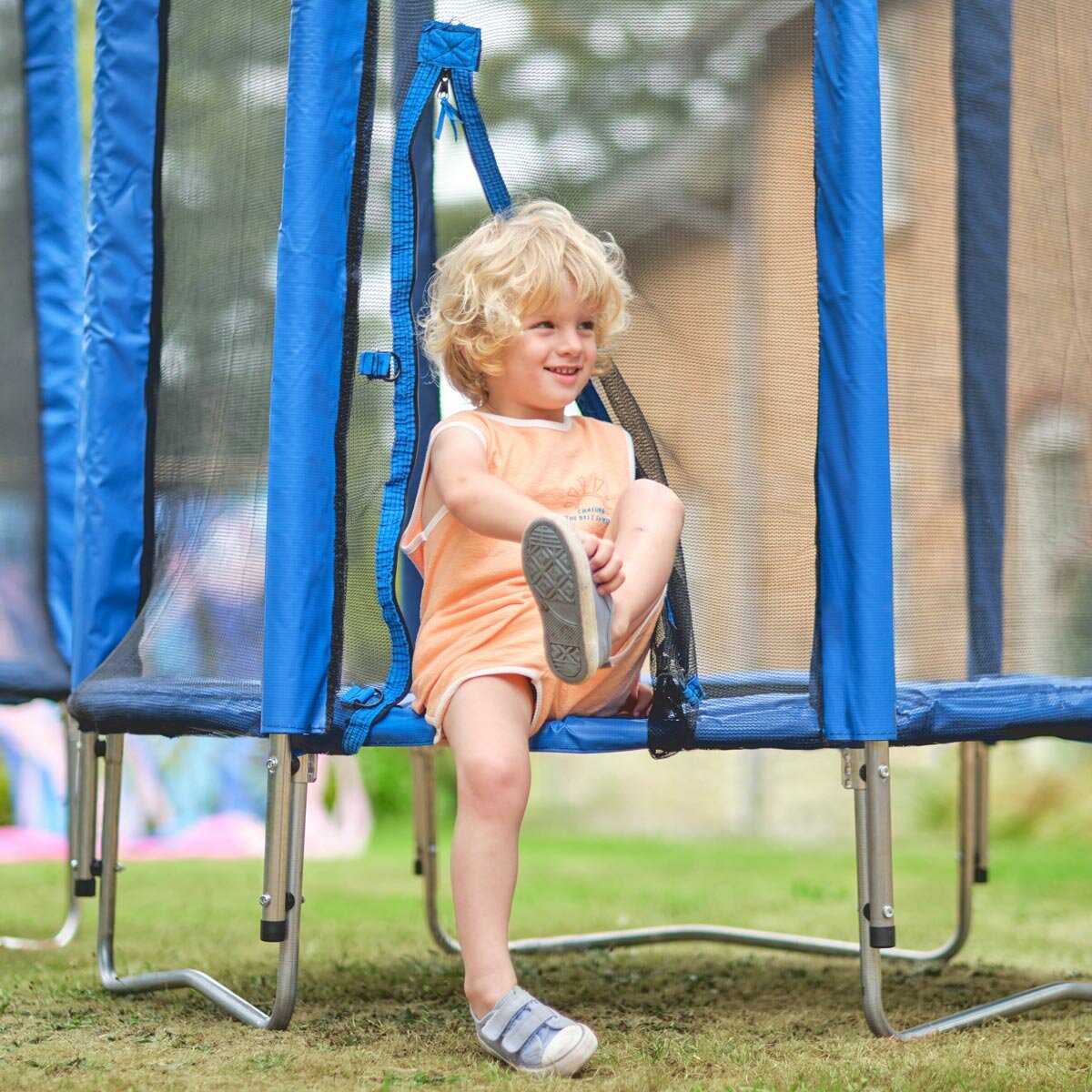 Lifestyle image of a child sat in the entrance to the trampoline, taking their shoes off