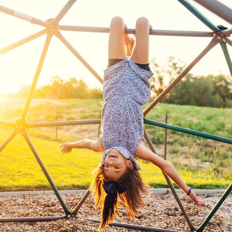 Lifestyle image shows a child hanging upside down on the Dome Climber