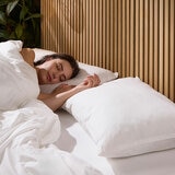 Two white pillows against a wooden headboard, with a person sleeping to showcase the comfort of the pillow Two white pillows against a wooden headboard, with a person sleeping to showcase the comfort of the pillow