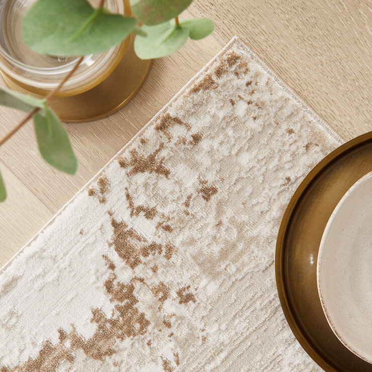 Textured rug with a distressed abstract pattern in beige, cream and light brown, showing irregular brushstroke-style detailing.