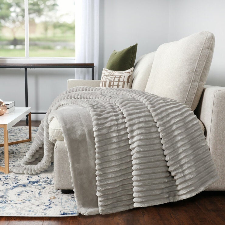 Light grey ribbed throw blanket draped over a cream armchair in a cosy living room Light grey ribbed throw blanket draped over a cream armchair in a cosy living room