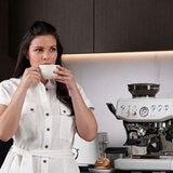 Lifestyle image of woman drinking coffee in front of Sage Express Impress Sea Salt