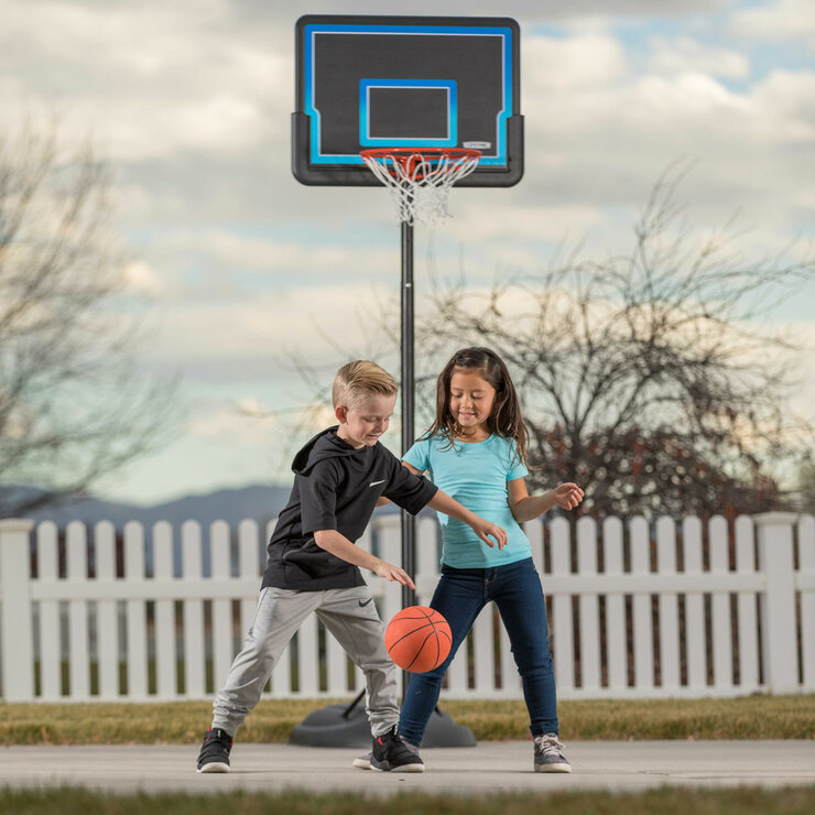 Lifestyle image of two children playing basketball with the Lifetime 32 Inch Youth Portable Basketball Hoop in the background