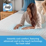 A fitted white mattress protector with a hexagonal quilted pattern on a neatly made bed in a modern bedroom
